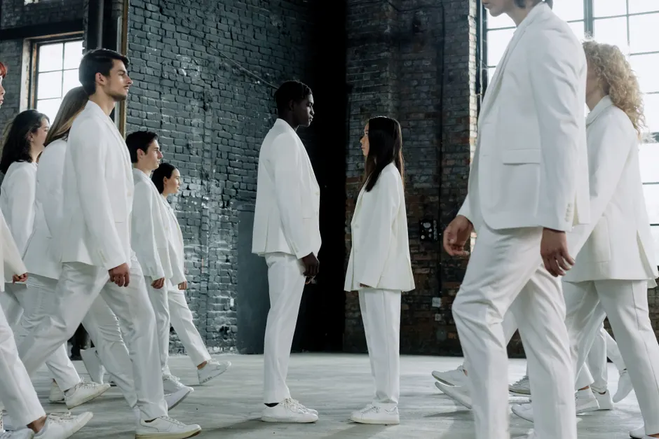 A diverse group in white suits face each other in an industrial setting, symbolizing equality.