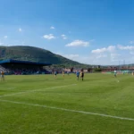 A lively Gaelic football match under blue skies with scenic hills in Ireland.