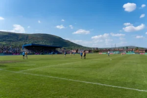 A lively Gaelic football match under blue skies with scenic hills in Ireland.