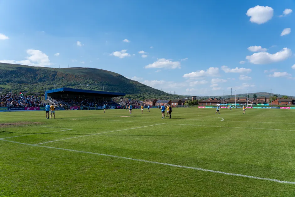 A lively Gaelic football match under blue skies with scenic hills in Ireland.