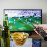 Ted Lasso saison 4 épisode 9 : date et heure en France A person holding a remote while watching soccer on TV with beer and snacks on the table.