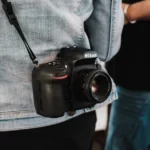 Australie : pourquoi certains lieux interdisent les lunettes connectées A professional camera hangs on a denim-clad person, showcasing photography essentials.