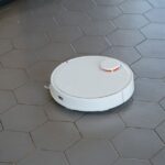 A sleek, white robotic vacuum cleaner operating on a hexagonal tiled floor.