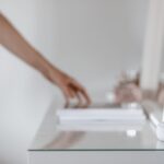 Quelle enceinte Echo choisir : Dot, Spot, Dot Max ou Studio? A smart speaker with a digital clock display placed on a minimalist desk setting, hand in background.