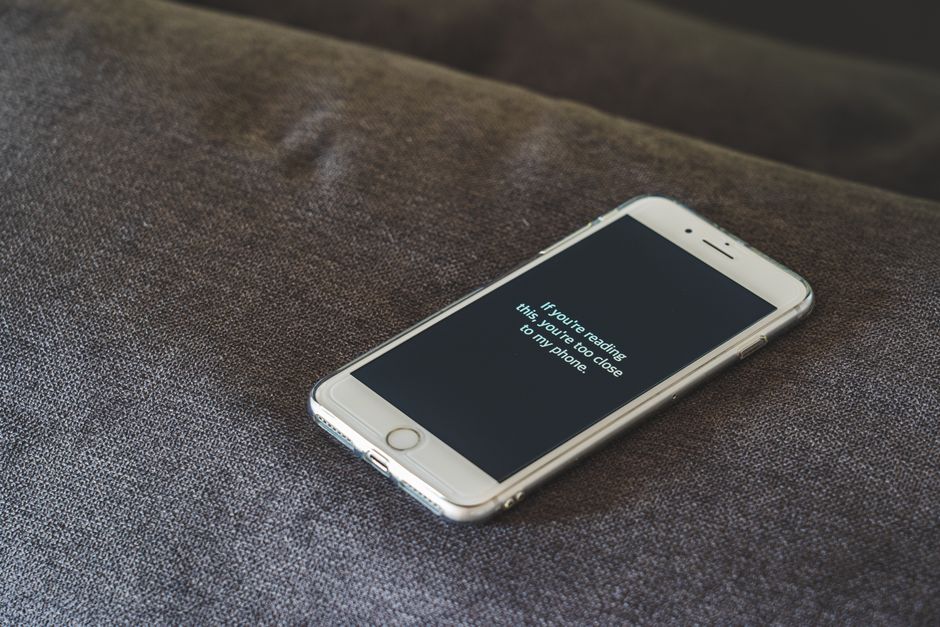 A smartphone with a humorous lock screen message placed on a grey couch, emphasizing privacy.