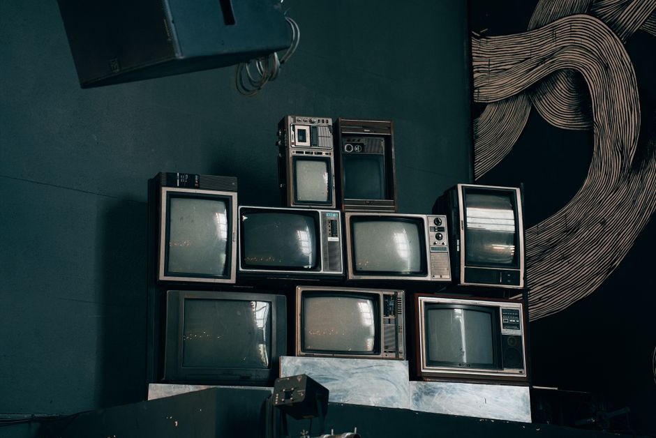A stack of vintage CRT televisions in a dimly lit modern room with abstract art.