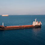 Aerial view of a cargo ship sailing in the open sea under clear skies, showcasing maritime transport.