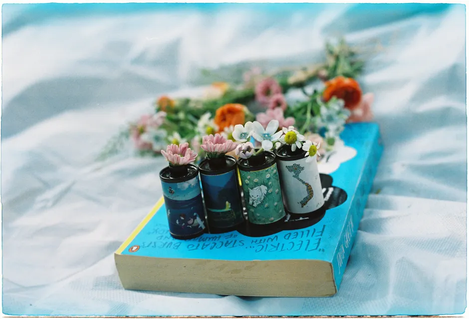 Artistic shot of vintage film canisters adorned with flowers on a book.