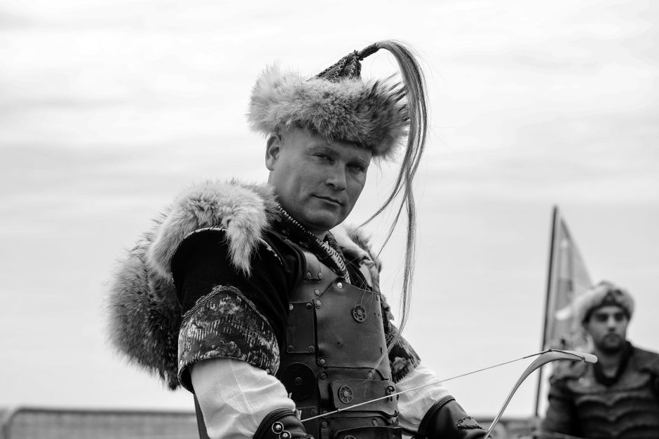 Black and white portrait of a medieval archer in traditional attire holding a bow.