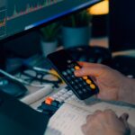 Gouvernance des agents IA : contrôler les données avant l’action Business analysis with calculator and computer monitor displaying financial graphs and charts.