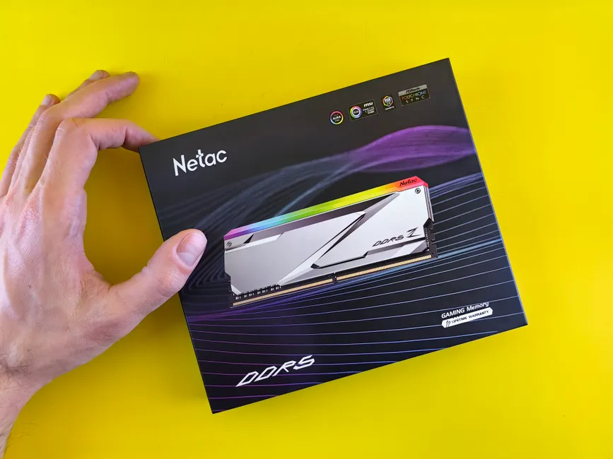 Close-up of a hand holding a Netac DDR5 gaming memory package on a yellow background.