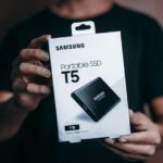 Samsung T7 1 To : rapide et pratique, mais pas universel Close-up of a person holding a Samsung T5 Portable SSD box, emphasizing modern technology.
