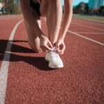 Marathon : une chaussure soldée n’est pas forcément la bonne Close-up of a woman tying her shoes on a running track, ready to sprint.