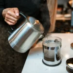 Des serveurs pour chauffer l’eau des foyers Close-up of pouring hot water into a French press in a modern kitchen setting.