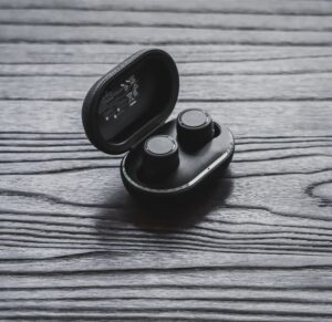 Close-up of true wireless earbuds in an open charging case on a textured wooden surface.