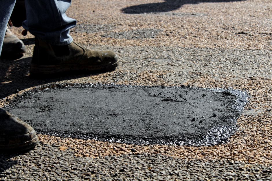 Close-up view of a freshly patched road section with work boots in South Africa.