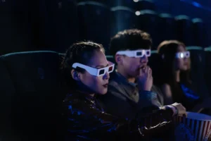 Friends enjoying a 3D movie night at the cinema, wearing glasses and eating popcorn.