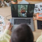 Affinity gratuit : ce que Canva ProSuite ajoute face à Adobe From above of crop faceless female photographer drawing on graphic tablet while editing photos on laptop at table with printed photos