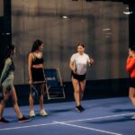 Billie Jean King Cup 2026 : calendrier, équipes et diffusion Group of women playing paddle tennis indoors, discussing strategies in an evening match.