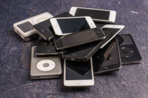 Heap of aged mobile phones with black screens and portable media players with symbols on buttons on gray background
