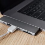 High angle of modern space silver laptop with USB type c multiport hub with plugged white cable placed on wooden table
