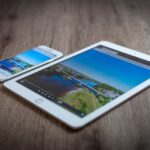 iPad mini 8 : caméra paysage, OLED et date incertaine iPad and iPhone showing a scenic landscape on a wooden table, highlighting portability and technology.