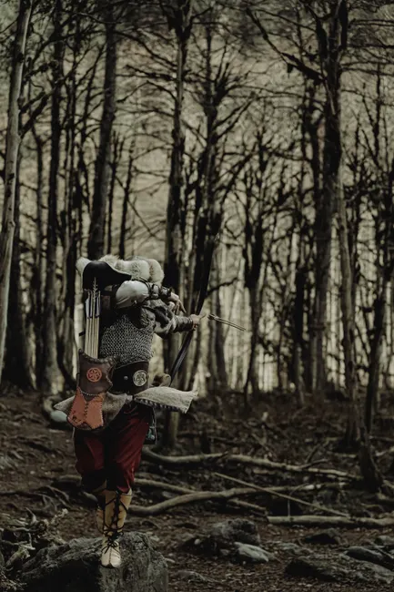 Medieval archer stands poised in a dense forest, aiming his bow and arrow.