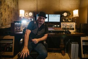 Music producer sitting in a modern recording studio with equipment and monitors.
