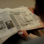 Amazon recontacte d'anciens salariés après plus de 30 000 suppressions de postes Person reviewing job listings in a newspaper, holding a pink marker for highlighting job ads.