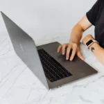 Le coût des tokens ne dit pas combien coûte vraiment votre IA Person using laptop with smartwatch on marble table, showcasing modern technology.