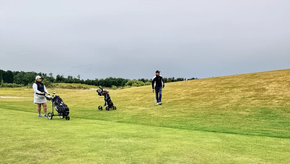 Two golfers on a lush green course in Skåne, Sweden, enjoying a leisurely game under a cloudy sky.