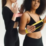 Bracelet sans écran Apple : ce qu'il faudrait vérifier Two women in workout attire using resistance bands for fitness training in a studio.