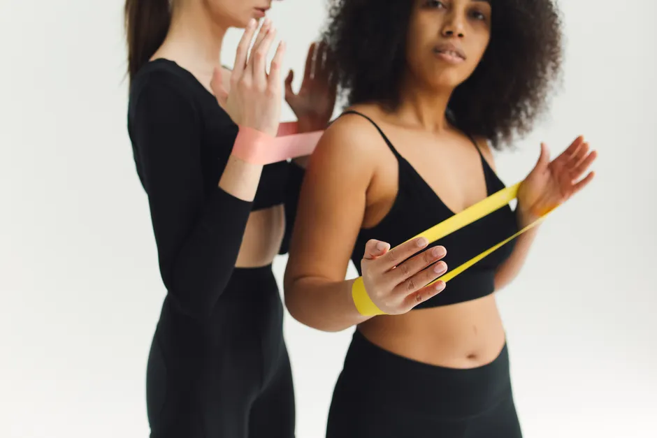 Two women in workout attire using resistance bands for fitness training in a studio.