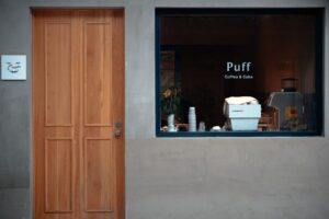 A modern cafe facade with a wooden door and a window displaying 'Puff Coffee & Cake' in Suzhou, China.