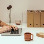 Des associations ont perdu des données après la fin d'une licence Microsoft 365 Hands typing on a laptop in a minimalist workspace with coffee and file organizers.