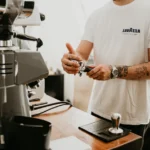 Lavazza Tablì : le café sans capsule est-il plus simple? Tattooed barista making espresso in a cafe with a professional coffee machine.