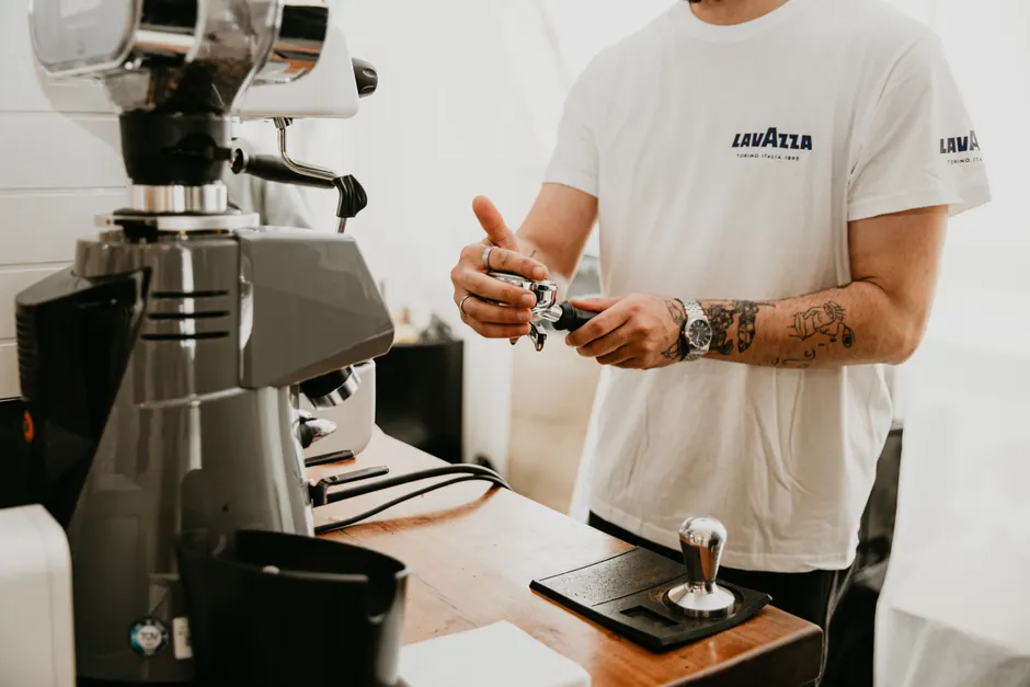 Tattooed barista making espresso in a cafe with a professional coffee machine.